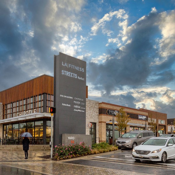 Yard 56 entrance, front view of Chipotle, large clouds, cars, and a person holding an umbrella.